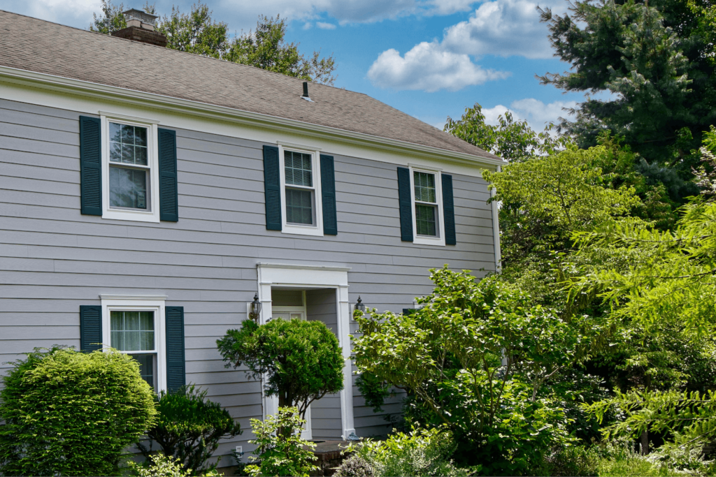 Classic home with gray siding and contrasting green shutters, surrounded by mature landscaping, demonstrating the value of exterior renovation for a high return on investment.
