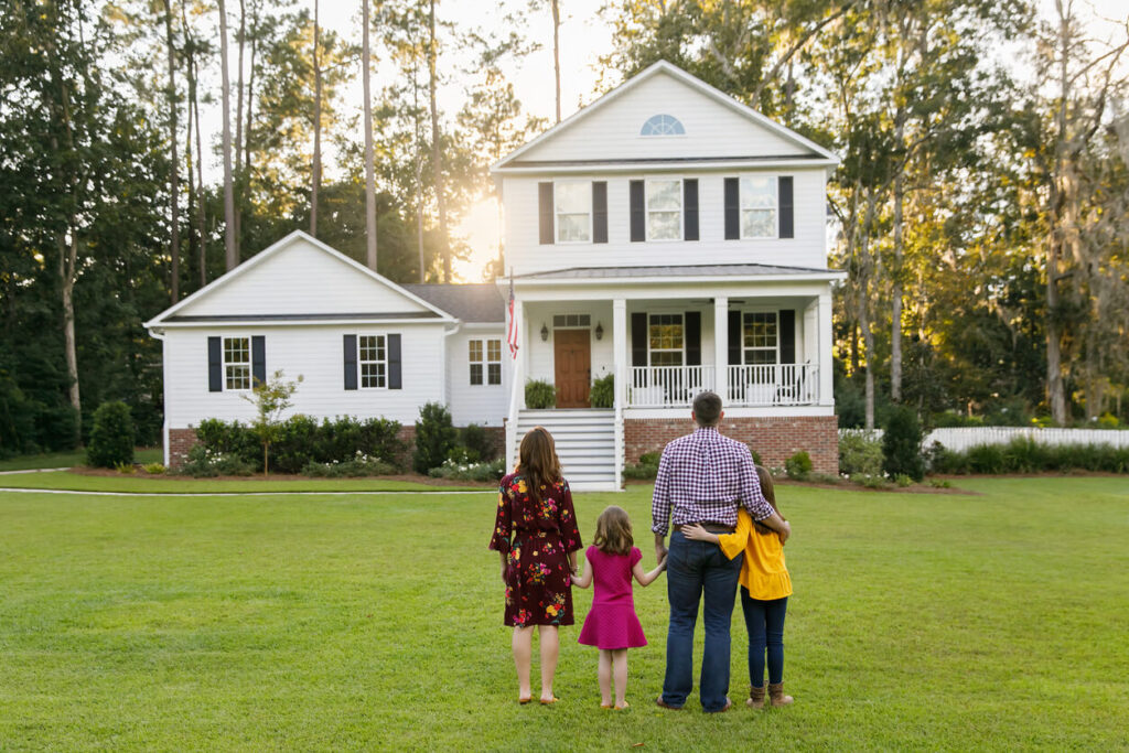 A family gazes at their charming white two-story home surrounded by lush greenery at sunset, exemplifying the quintessential American dream and illustrating how a well-maintained exterior significantly boosts curb appeal.