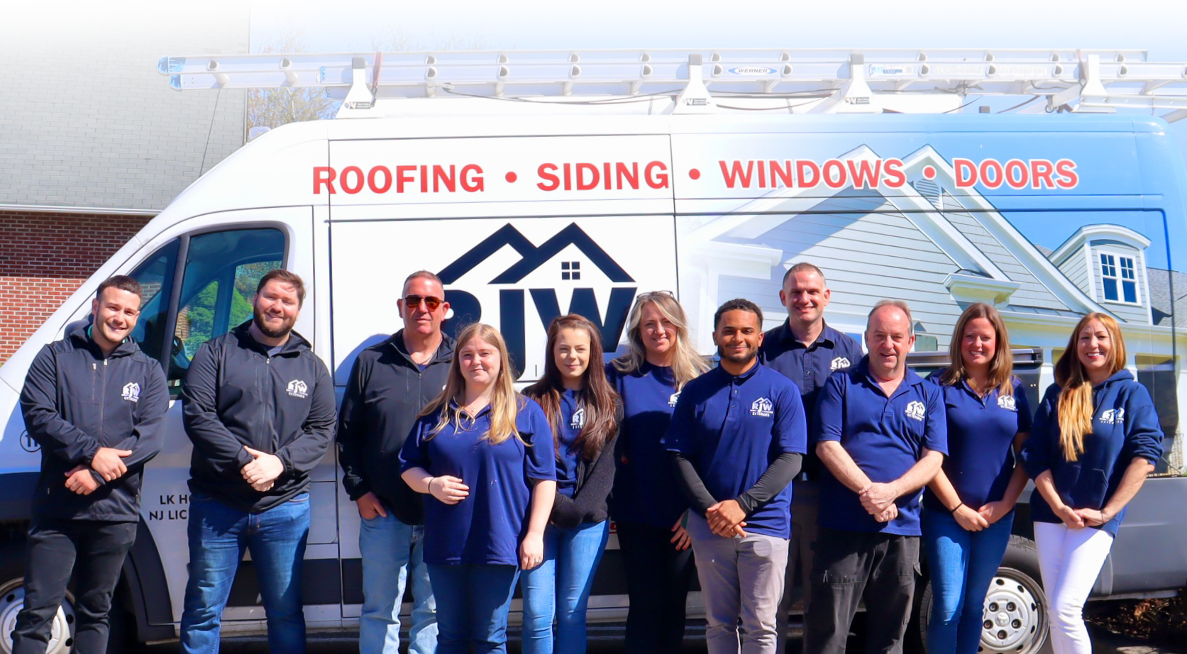 Group of eleven people in company uniforms standing in front of a branded van advertising roofing, siding, windows, and doors services.