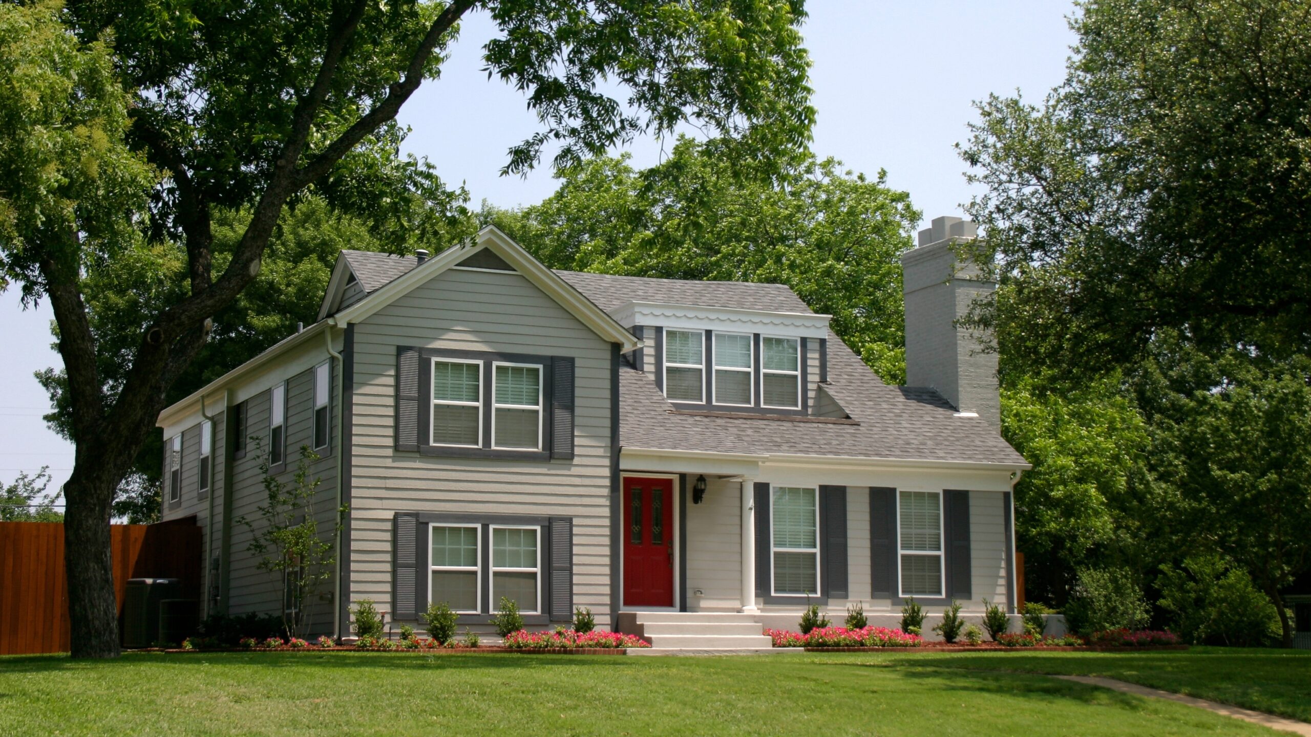 A large home with tan siding, green shutters, and a gray shingle roof