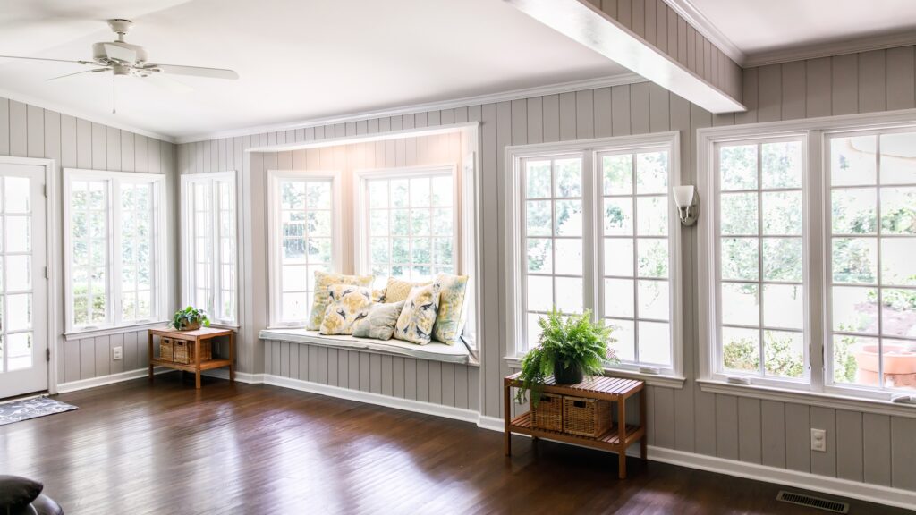 A well-lit sitting room with a wall of windows, a window seat, and wood floors