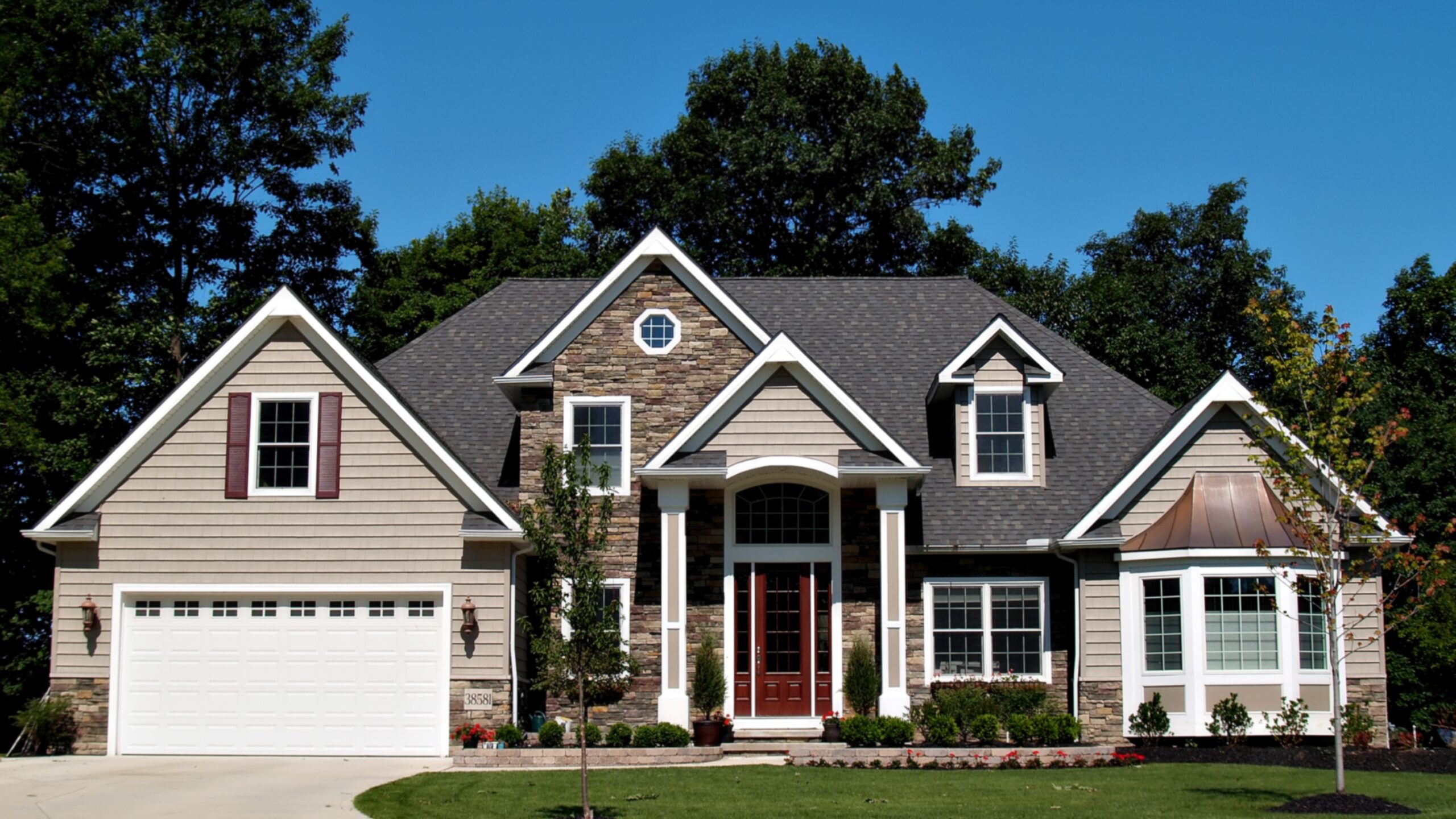 A home with tan and stone siding and white trim surrounded by trees