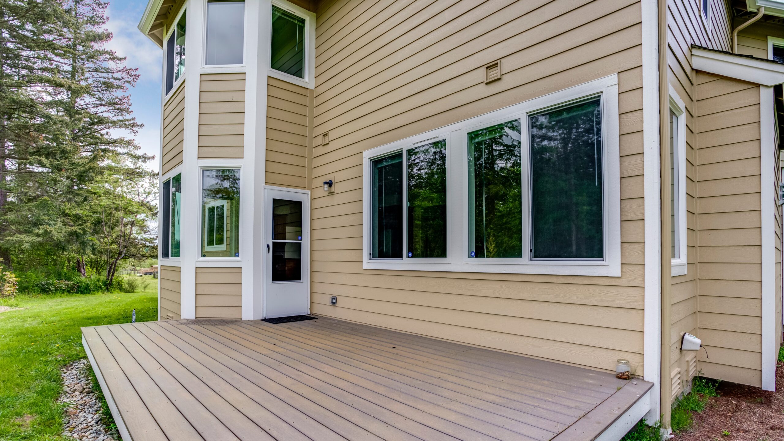 The backside of a yellow-sided home with white trim and newly installed replacement windows