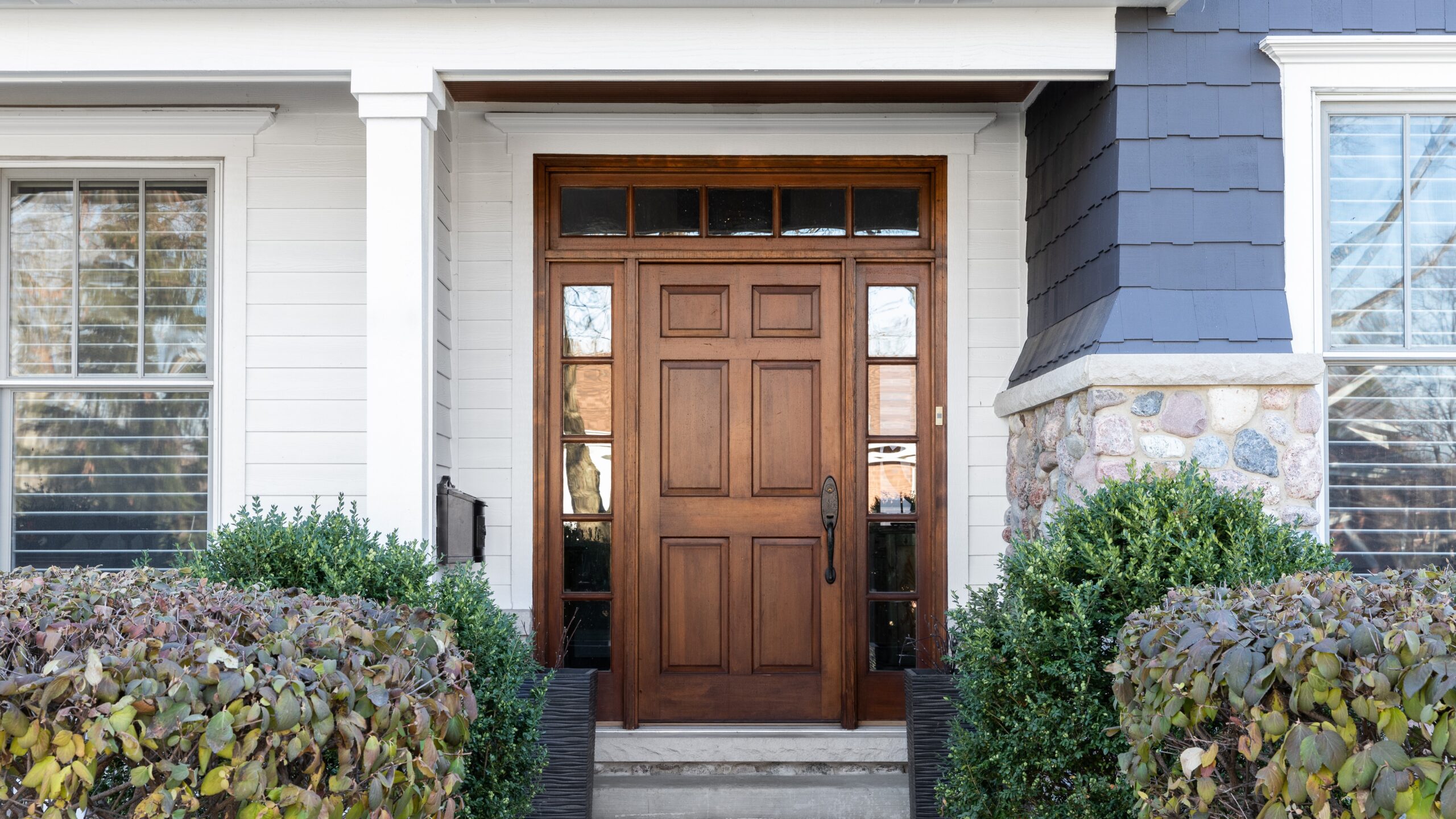 Close view of a home with a paneled wood door with transom windows and sidelites