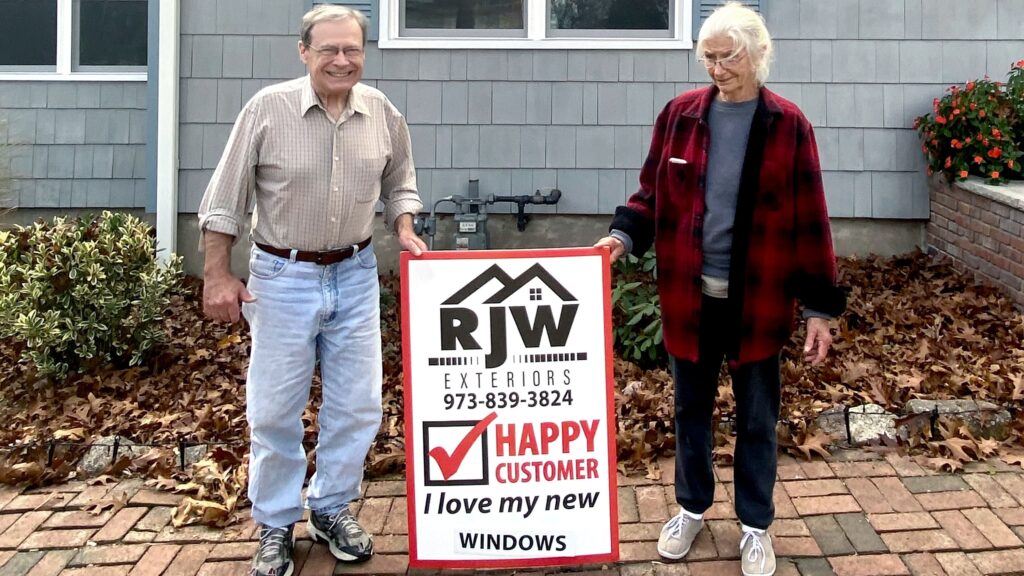 Mark and Genny outside their home with an RJW Exteriors sign after their window replacement project