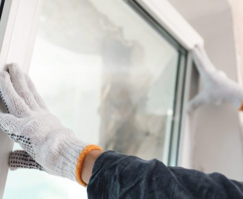 A window installer with white gloves places a replacement window in the opening