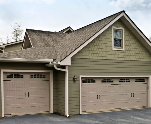 A wide view of the side of a suburban home clad in two shades of green Hardie Board in two different styles