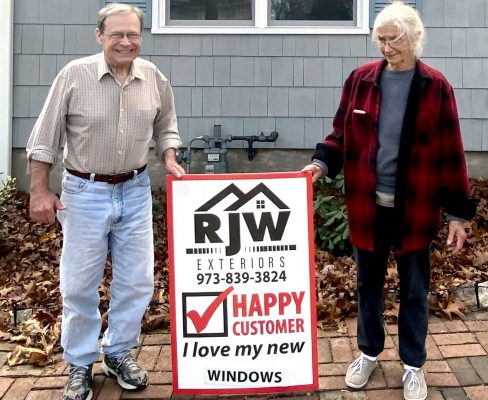 Mark and Genny outside their home with an RJW Exteriors sign after their window replacement project