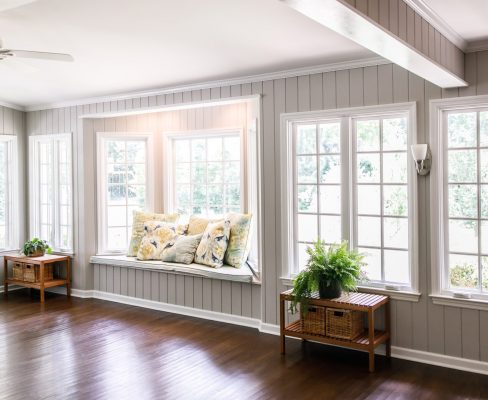 A well-lit sitting room with a wall of windows, a window seat, and wood floors